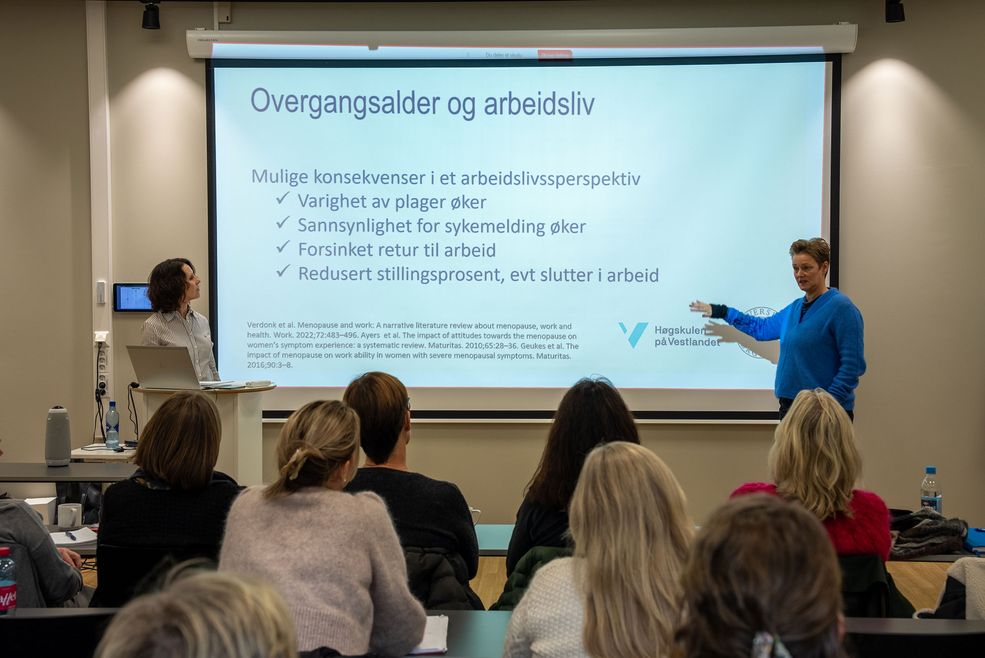 Anette Fagertun og Una Ørvim Sølvik presenterer og står foran et lerret 