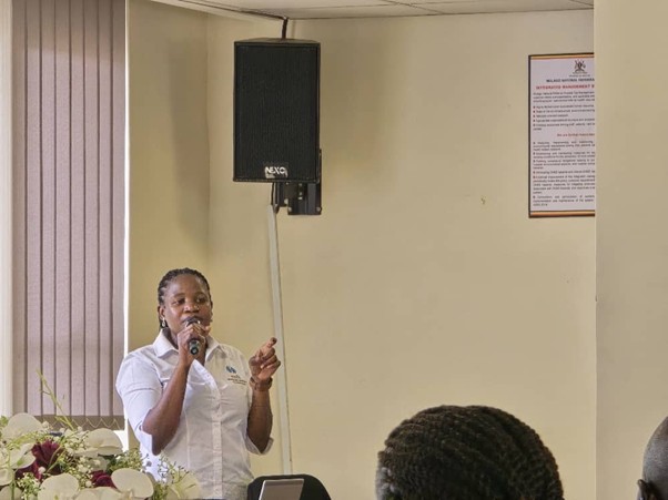 Woman in white shirt standing and talking. Holding microphone and speaking, while pointing. 