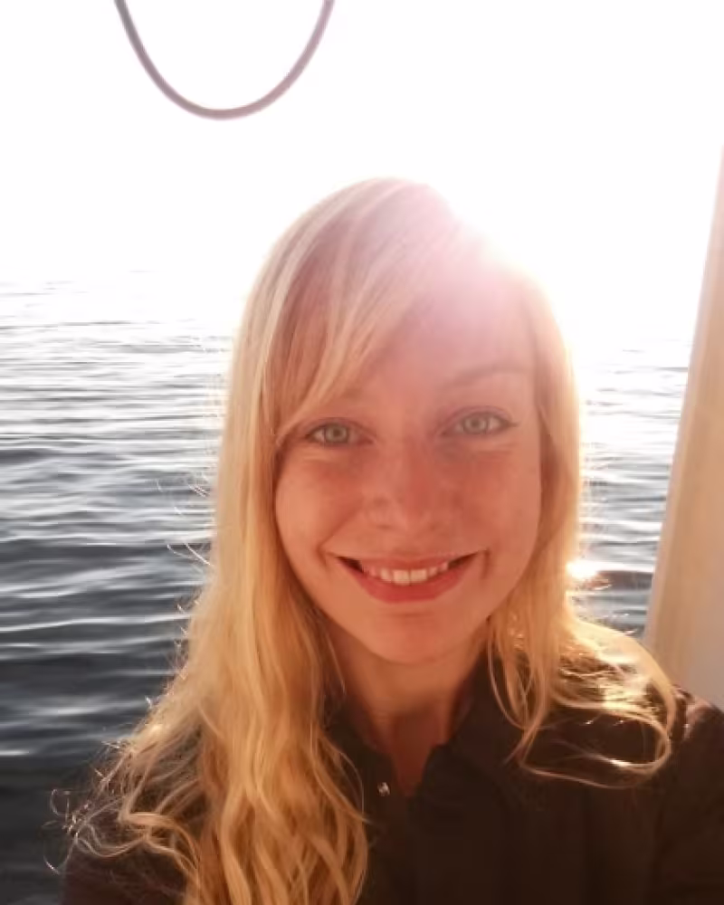 young woman smiling on a research cruise with sun behind