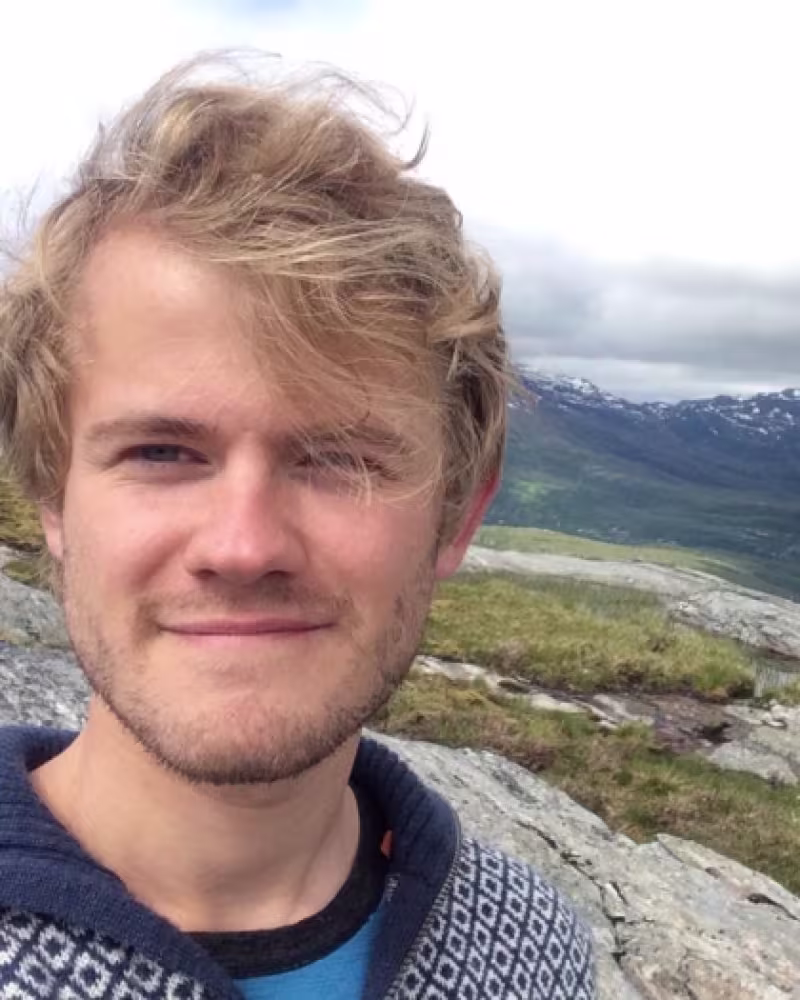 young man with blond hair smiling on top of a mountain
