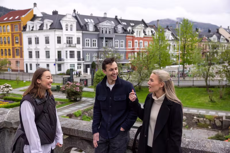Tre studenter står og snakker sammen på Nygårdshøyden i Bergen sentrum.