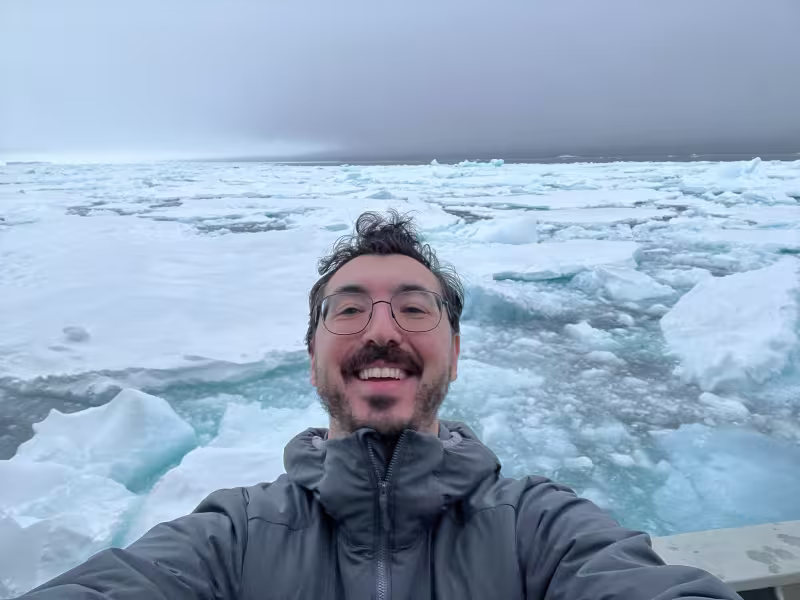 young man with dark hair takes smiley selfie in front of sea ice