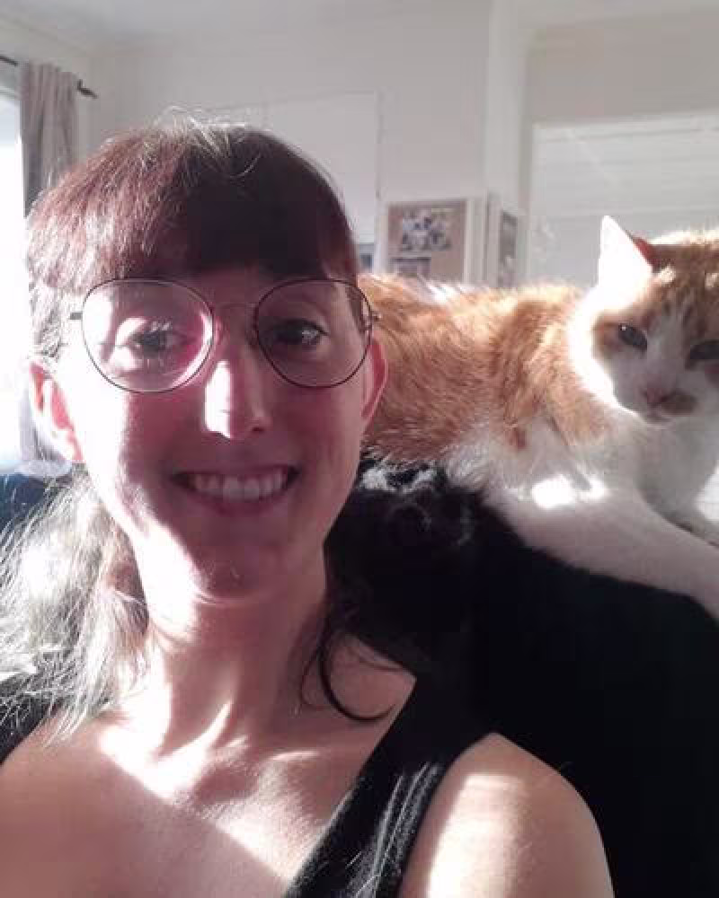 Girl with dark hair and glasses with ginger and white cat on shoulder
