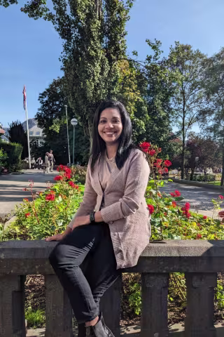 Youndg woman smiling at camera in the sushine with greenery behind