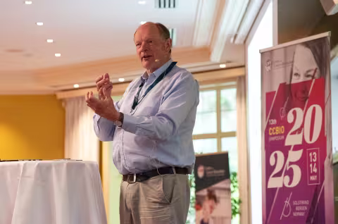 Sir David Lane standing on stage, speaking, waving his hands.