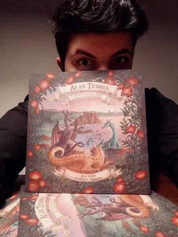 Monica holding the Alia Terra childrens' book with colourful and fantastic illustrations of dragons.
