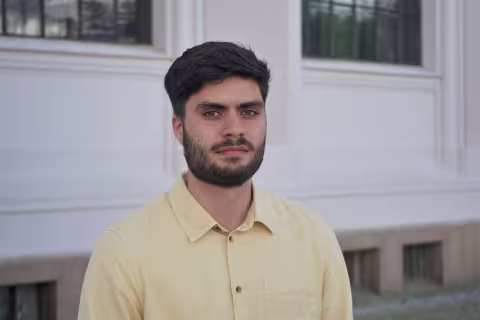 Picture of Soran Dahl. Male with dark hair and short beard, standing outside in front of university building.