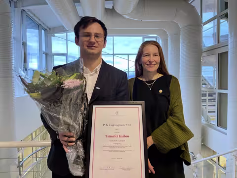 A male and female smiling to the camera with flowers and an award