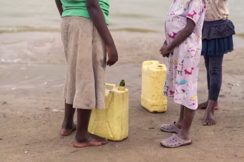 Picture of some people standing in a beach in Africa. We can only see their lower bodies. 