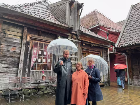 3 people with umbrellas standing in front of old timber buildings. 