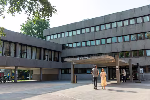 Bilde av HF-bygget (Humanistisk fakultet) ved Universitetet i Bergen. To mennesker kan ses gående mot hovedinngangen.