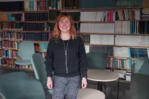 Betti shown in a room full of books. She is smiling. 