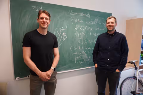To menn foran en tavle med matematiske utregninger.