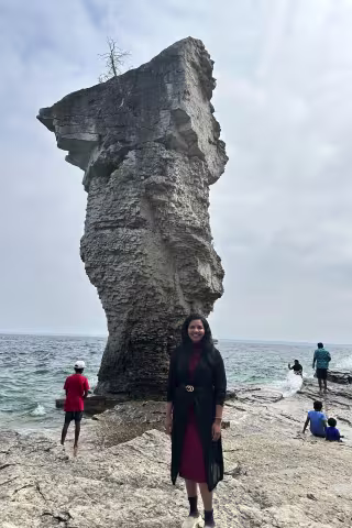 Young woman standing at the coast with rock formation behind