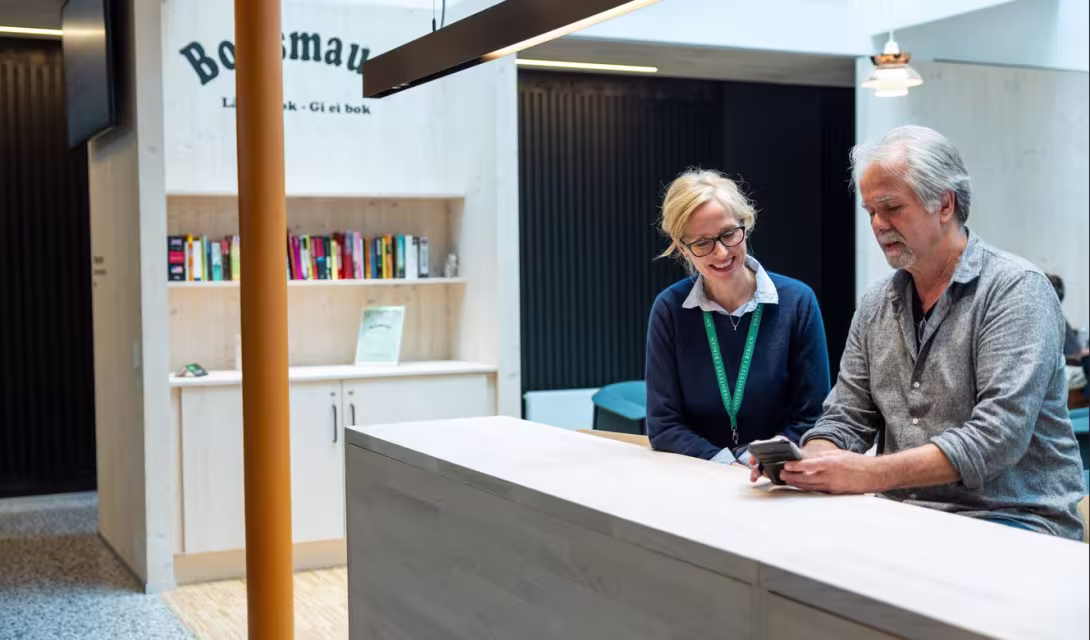 Mann og dame står bak en høy disk Mannen viser noe på en mobilteefon 