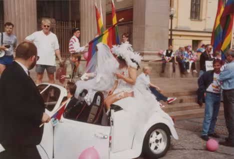 Gammelt bilde av noen i en bil med regnbueflagg i bakgrunnen