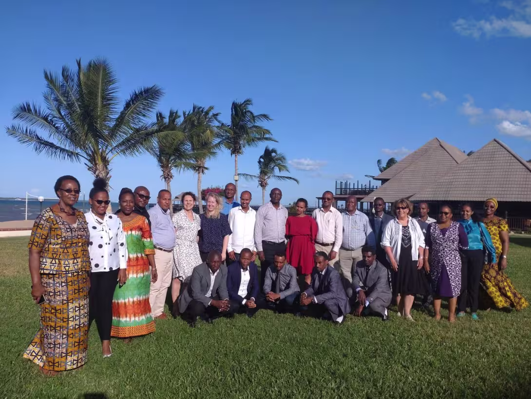 Group photo of participants outside on a lawn, with palmtrees and huts behind them. The sea can be seen in the background.
