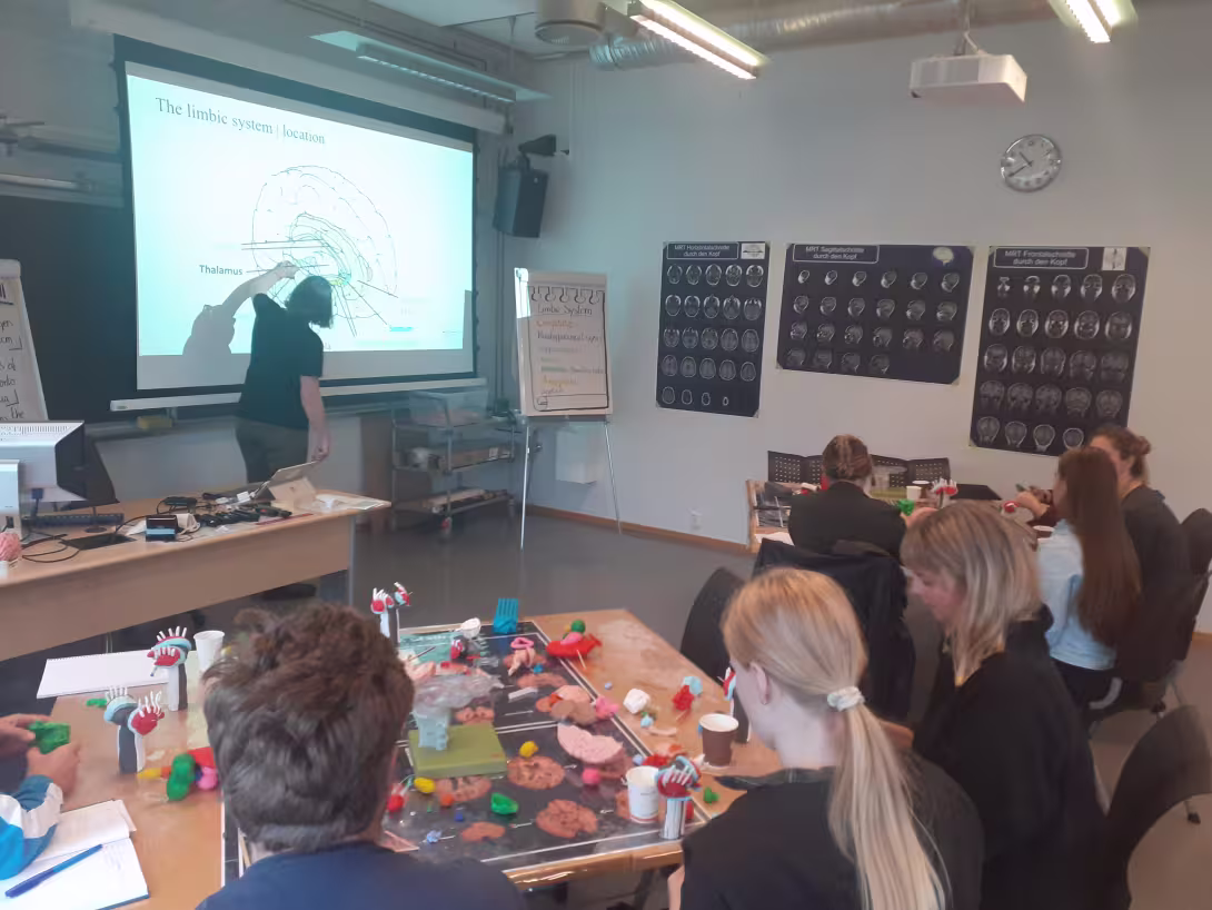 En foreleser er vendt mot prosjektorlerret og forklarer noe om hjernen til studenter som sitter i rommet