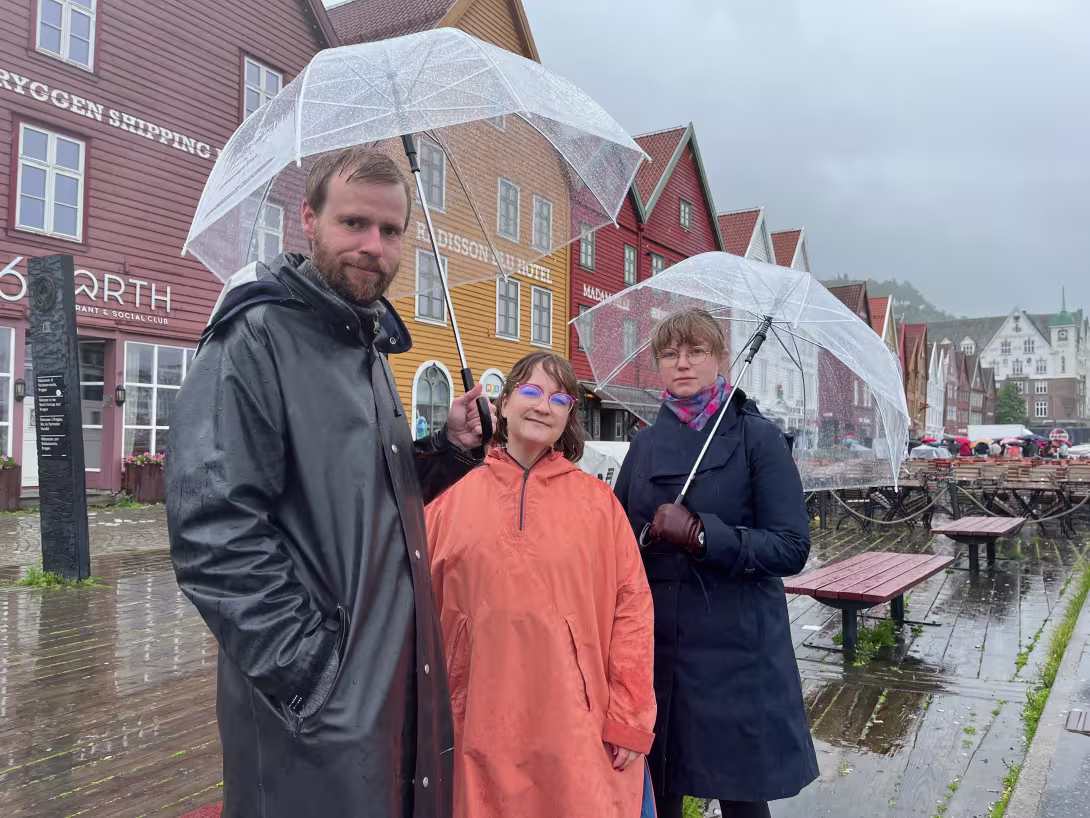 three people standing under umbrellas in front of Bryggen in Bergen
