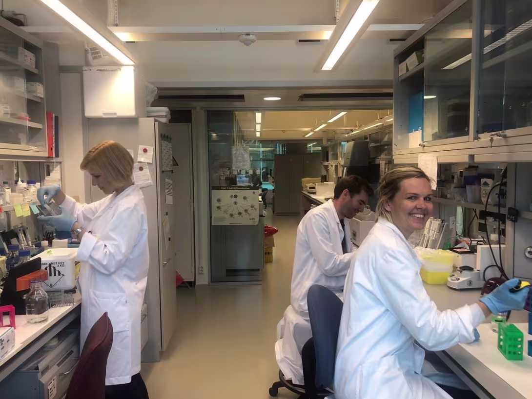 Tre av gruppens medlemmer som arbeider på labben. Alle smiler. 