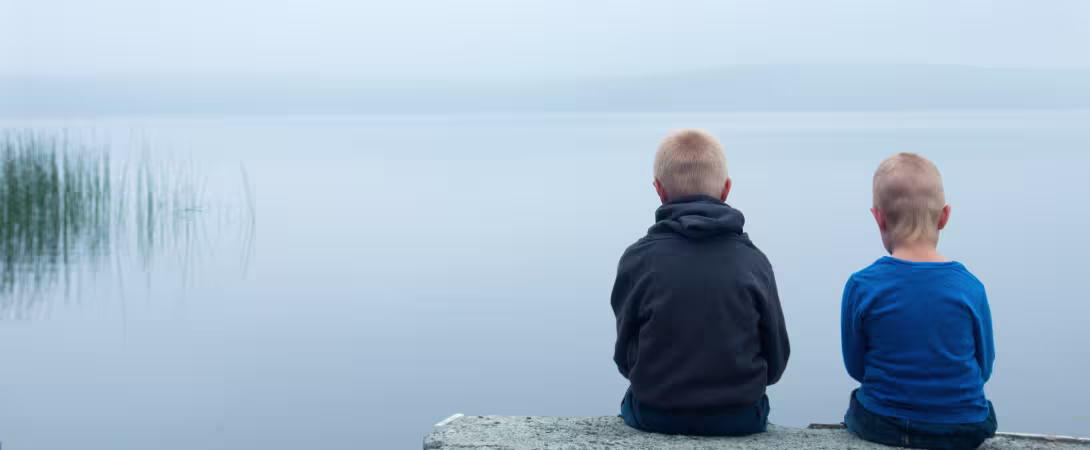 To triste smågutter sitter ved et vann. Illustrasjonsbilde til deltidsstudiet Barn som pårørende ved UiB.