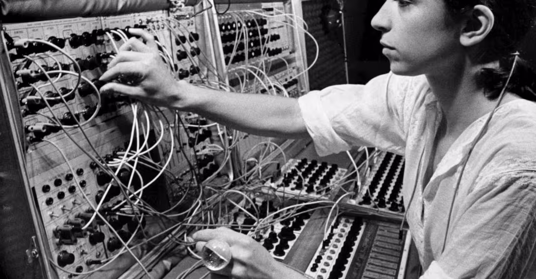 A black and white photo of a young woman operating a modular synthesizer