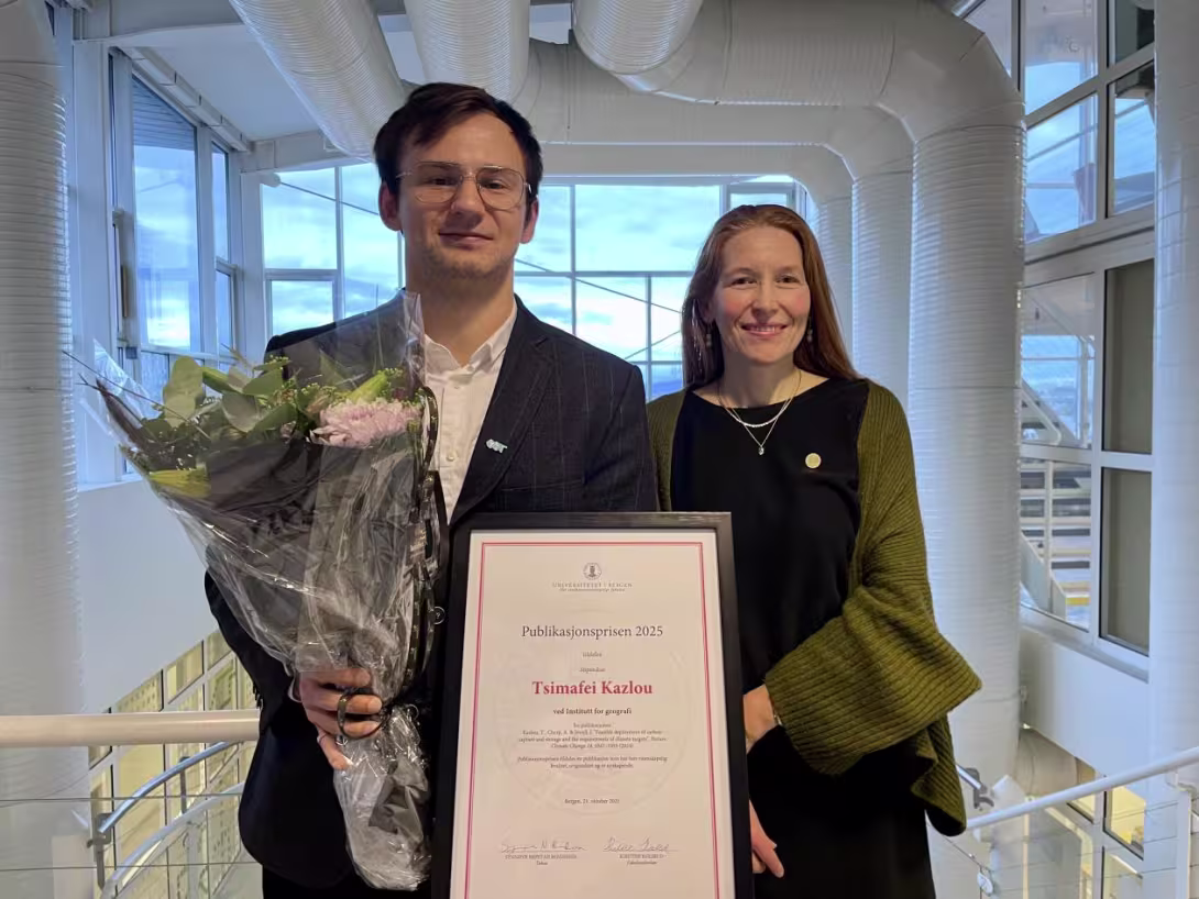 A male and female smiling to the camera with flowers and an award