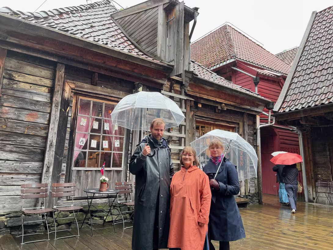 3 people with umbrellas standing in front of old timber buildings. 