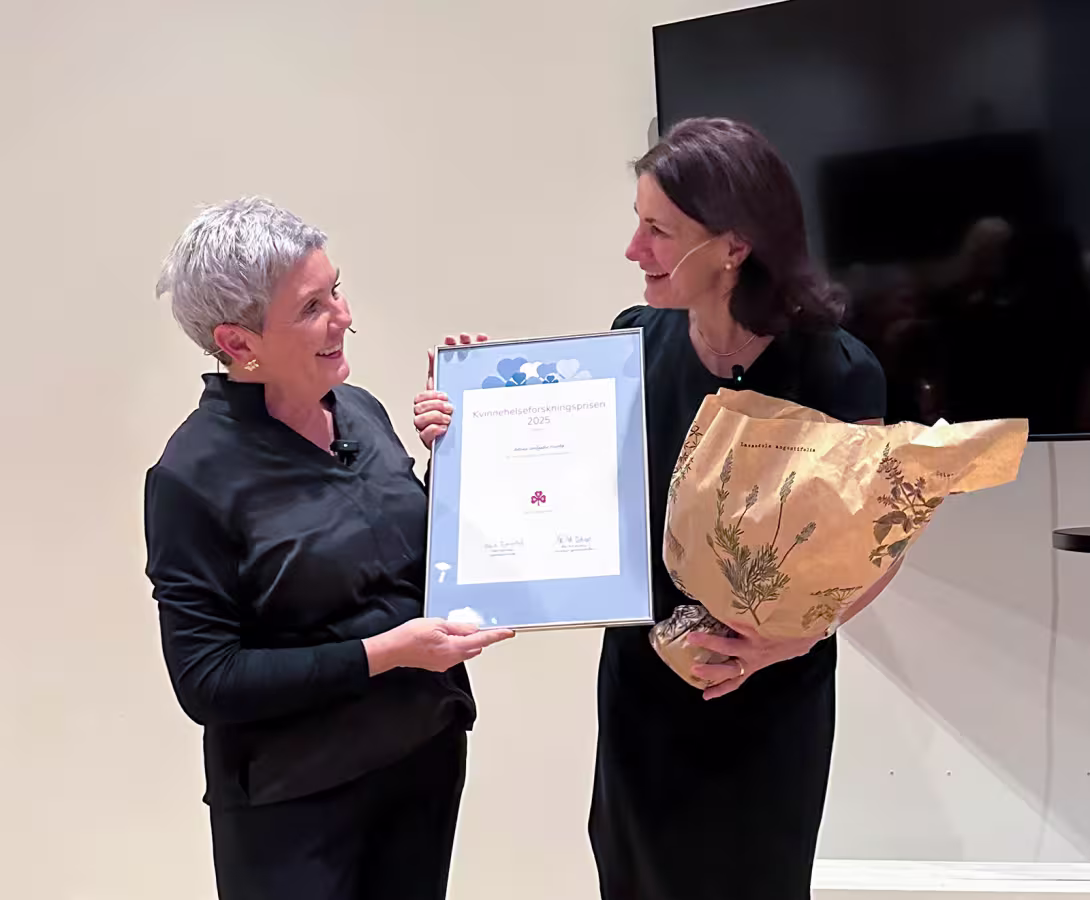 To kvinner på scenen, der den ene gir et diplom og blomster til den andre.