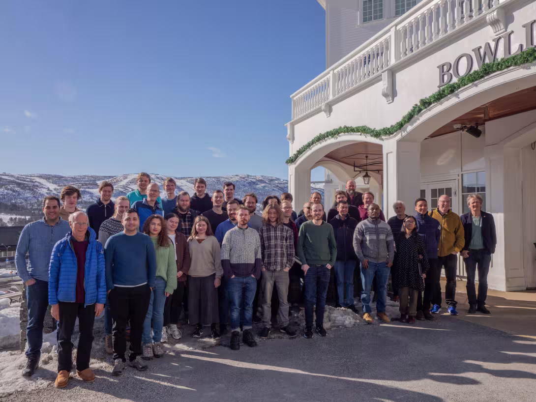 Large group of people posing outside hotel with mountains in the background.