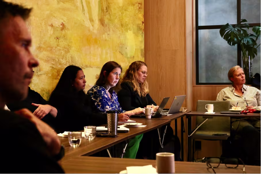 mennesker rundt bord, noterer og lytter til presentasjon
