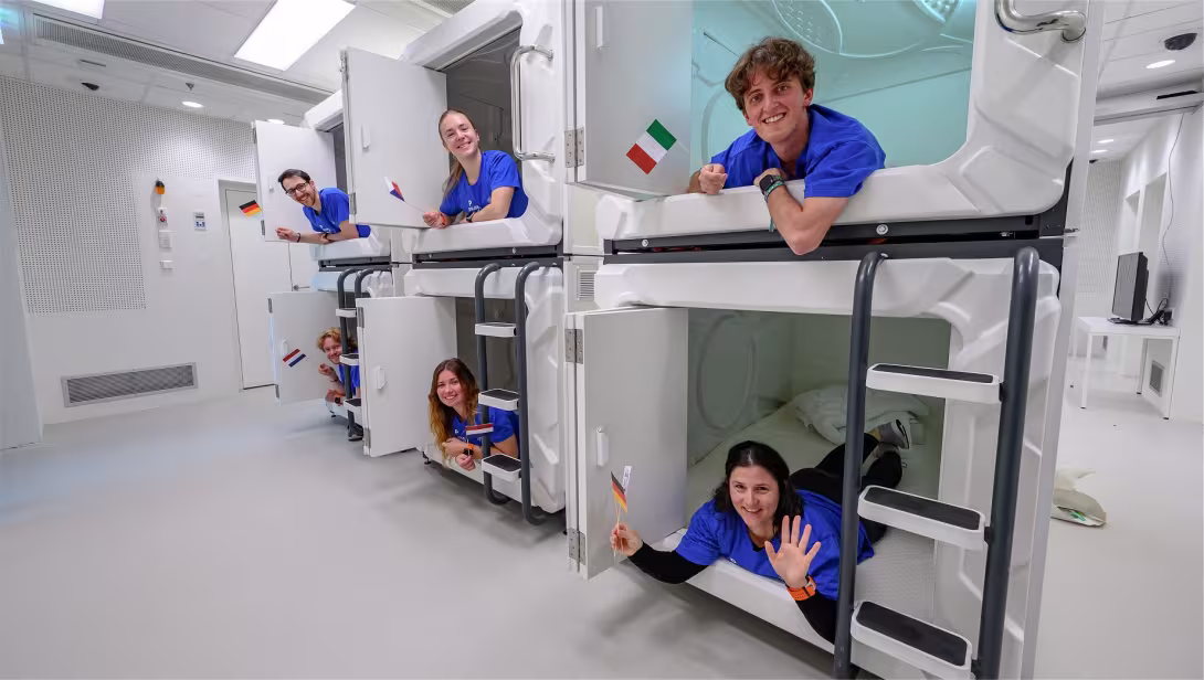 Six young astronauts waving from each their sleeping pod.