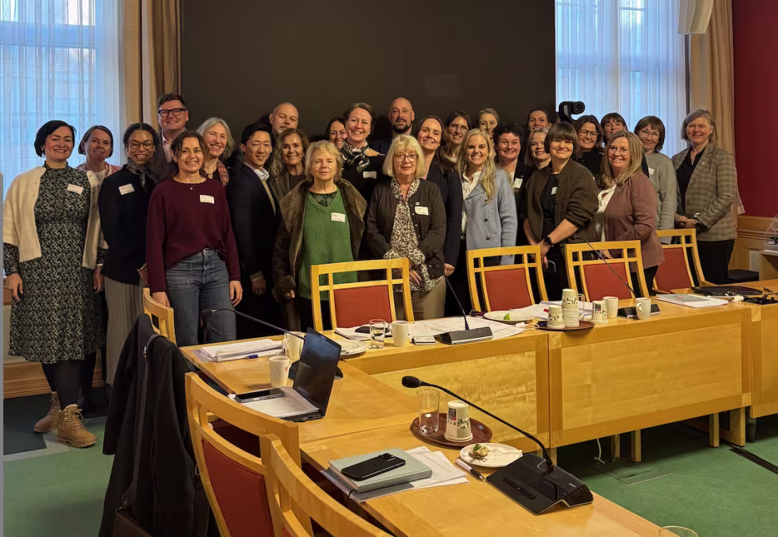 Bilde av en gruppe mennesker som står oppstilt bak et konferansebord