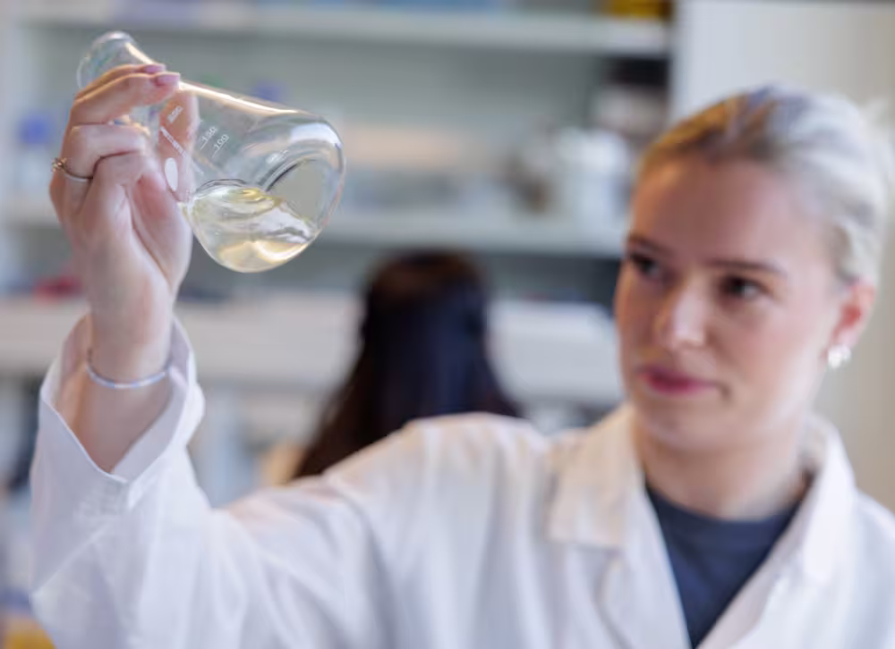 Illustrasjonsbilde: Student på lab holder opp og studerer innholdet i en kolbe. 