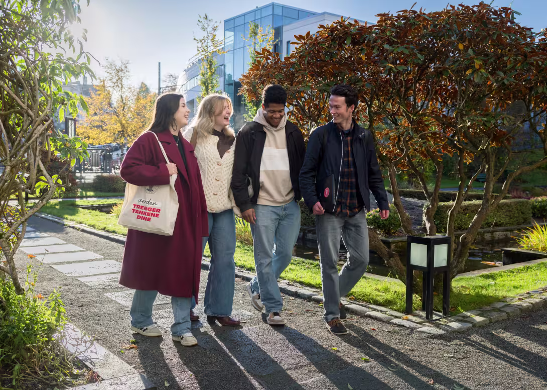Four students walking in the museum garden. The student centre is visible in the background.