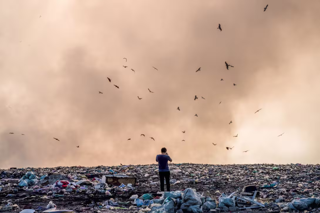 Man stands in pile of plastic litter and takes a photo