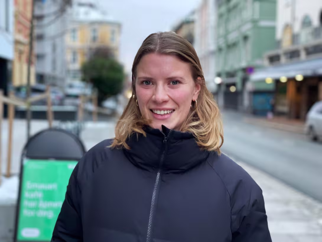 Blond kvinne med boblejakke, med bybilde i bakgrunnen